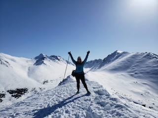 Amy raising her arms on top of Near Point peak with snowy mountains all around.
